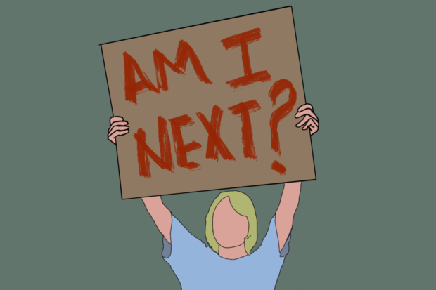 A teenage holding up a sign that says "Am I next?"