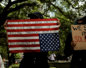 One of the protesters from the Houston demonstrations holding an upside down American flag with the words, "No flag is large enough to cover the shame of killing innocent people,” sprawled across it. | Mikol Kindle Jr./The Cougar