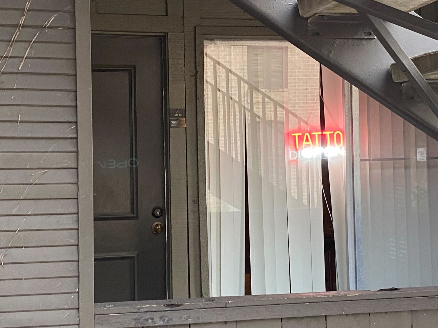View of an apartment window with a glowing neon red and white sign inside, reading "tattoo open."
